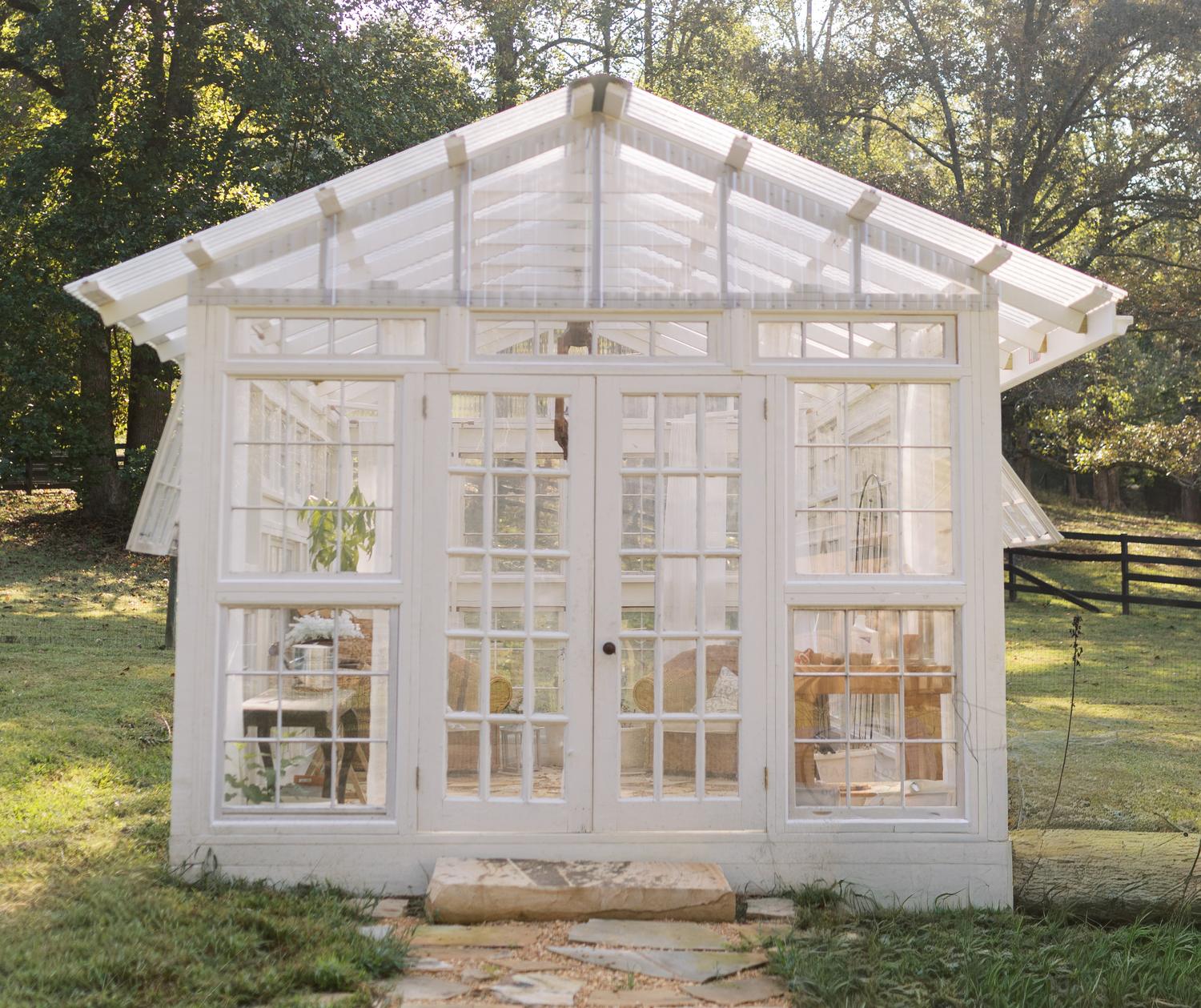 The white timber greenhouse at Chipper Ridge with sun breaking over the roof and a flagstone path leading to the doors